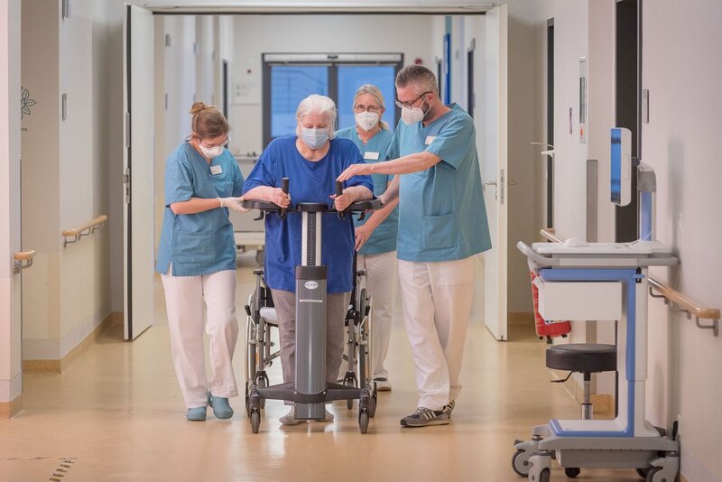 Eine Patientin wird kurz nach einem Schlaganfall von zwei Physiotherapeutinnen obilisiert