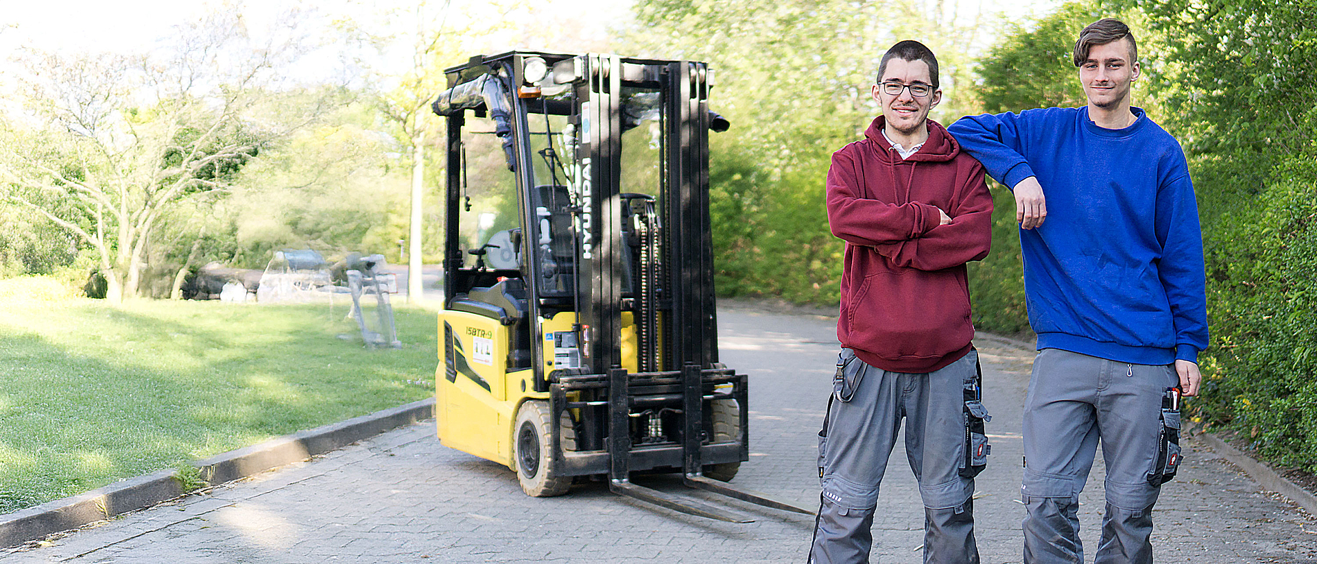 Zwei Auszubildende stehen vor einem Gabelstapler.