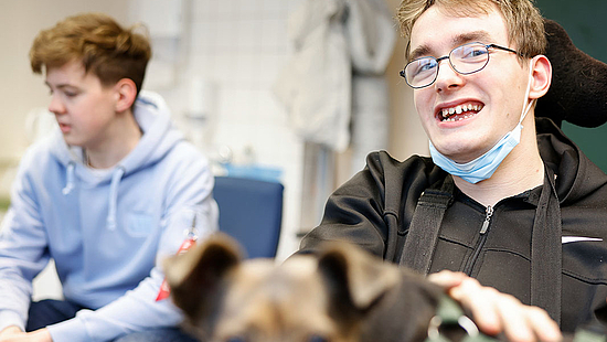 Ein junger Mann mit Behinderung und im Rohlstuhl sitzend lächelt in die Kamera