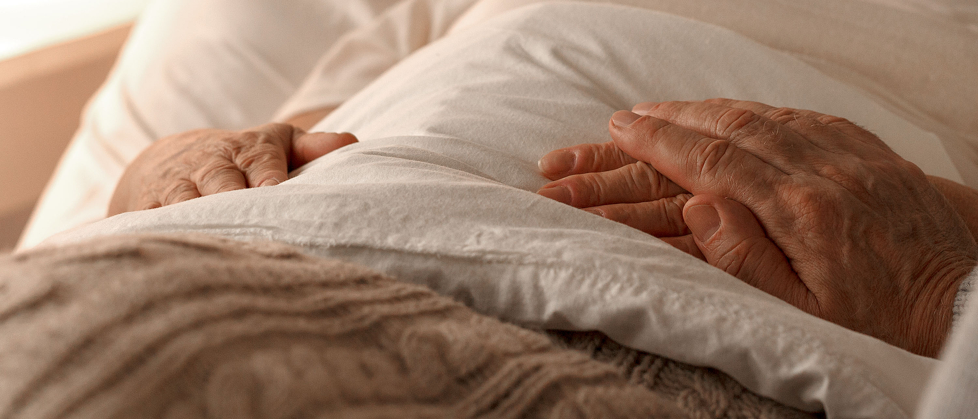 Bild zeigt zwei Hände eines älteren Menschen im Bett liegend.