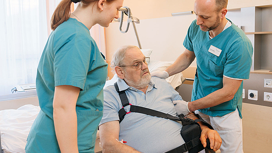 Eine Physiotehrapeutin und ein Physiotherapeut unterstützen einen Patienten mit einer operierten Schulter.