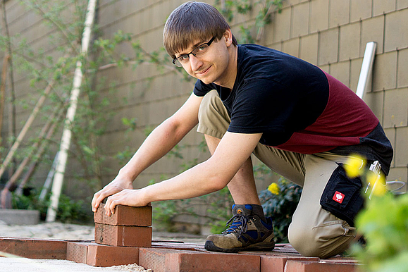 Ein Gärtner legt Pflastersteine auf einen Weg.