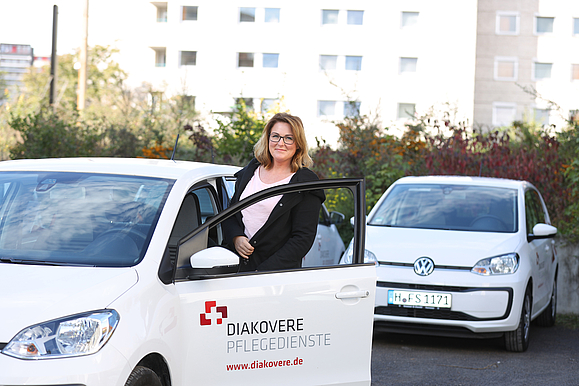 Pflegedienstmitarbeiterin, die in ein Auto des ambulanten Dienstes steigt.